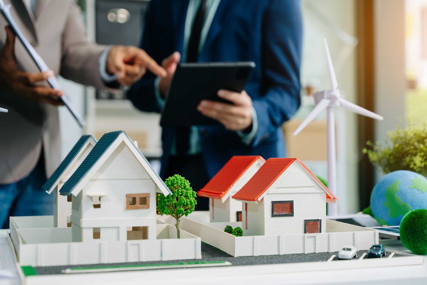 Dos personas apuntando hacia una tablet, de pie detrás de una maqueta