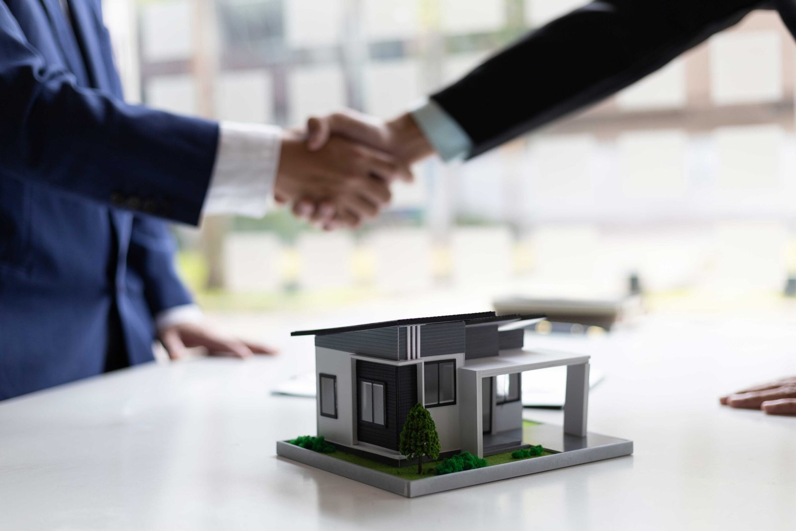 Dos personas estrechando manos. Al frente la maqueta de una casa.